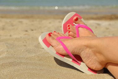 Womans feet with flip flops on the sand clipart