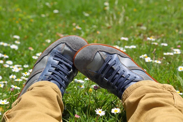 Voeten in schoenen op groene veld met bloemen — Stockfoto