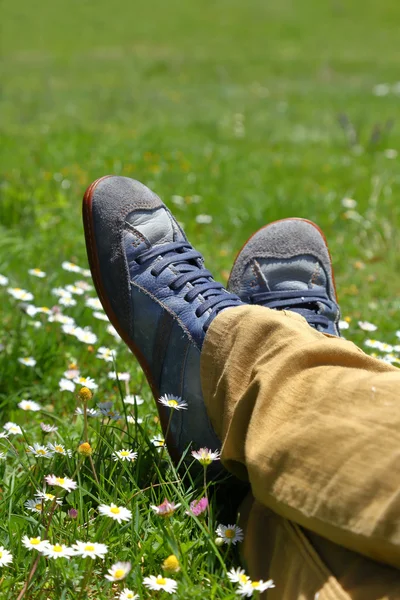 Voeten in schoenen op groene veld met bloemen — Stockfoto