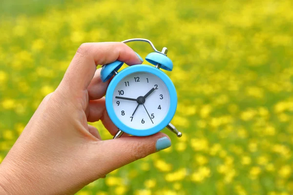 Mano sosteniendo un reloj despertador con fondo de naturaleza abstracta — Foto de Stock