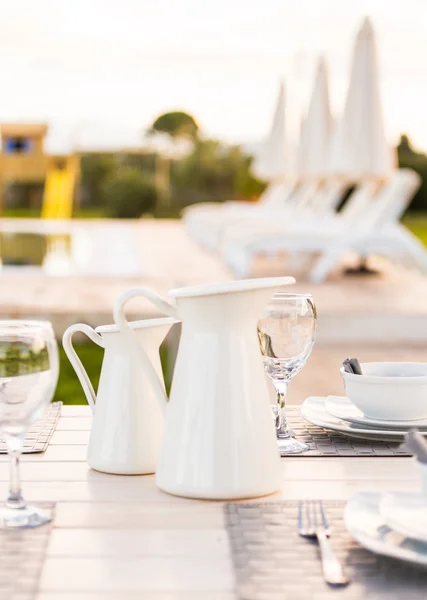 Jarros de mesa brancos elegantes, tigelas, pratos e copos de vinho colocados na mesa — Fotografia de Stock
