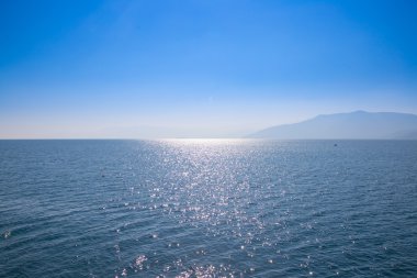 Mavi gökyüzü ve suları, uzak bir diyarda siste gizlenmiş ile deniz manzarası.