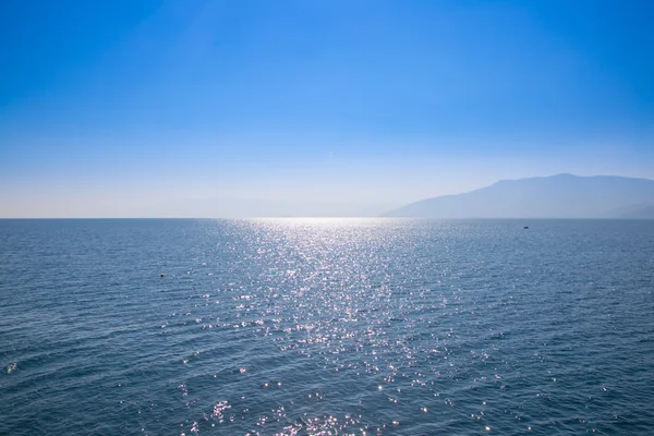 Mavi gökyüzü ve suları, uzak bir diyarda siste gizlenmiş ile deniz manzarası. — Stok fotoğraf