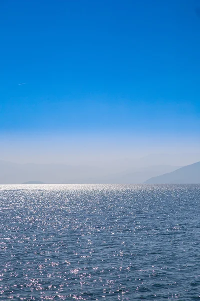 Морський пейзаж з блакитним небом і водами, з віддаленою землею, захованою в тумані . — стокове фото
