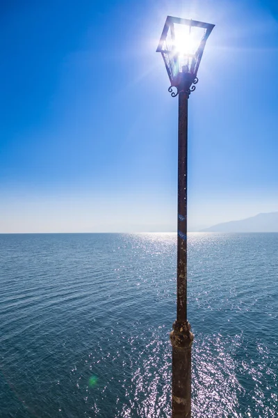 Old street lamp with sunbeams coming through, with seascape background. — Stock Photo, Image