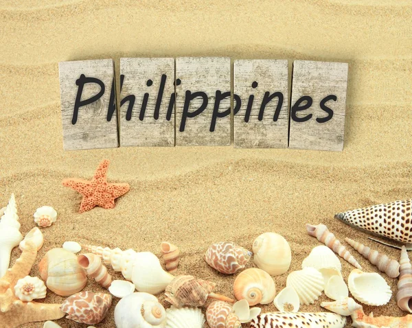 Filipinas en piezas de madera con conchas de mar y arena — Foto de Stock