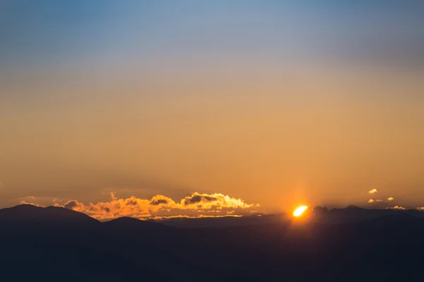 Pôr do sol / nascer do sol com céu colorido vívido, nuvens e montanhas silhuetas escuras . — Fotografia de Stock