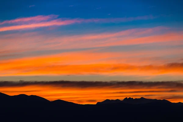 Západ slunce / svítání s živé barevné nebe, mraky a hory temné siluety. — Stock fotografie