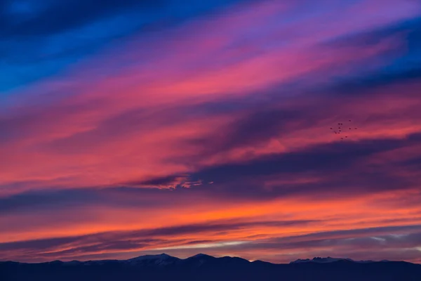 Západ slunce / svítání s živé purpurové nebe, mraky a hory temné siluety. — Stock fotografie