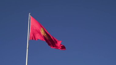 Kırgızistan 'ın kırmızı bayrağı rüzgarda dalgalanıyor, 40 vatozlu ve merkezi tunduk amblemli altın bir güneş, canlı bir gökyüzü altında ulusal kimliği, birliği ve kültürel mirası simgeliyor..