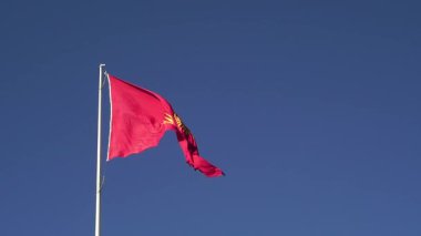 Kırgızistan 'ın birliğini, mirasını ve göçebe kültürünü temsil eden 40 ışın ve tunduk desenli merkezi altın bir güneşe sahip kırmızı bayrak, açık gün ışığında belirgin bir şekilde çırpınıyor..