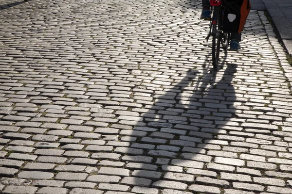 Велосипедист и тень на мощеных камнях — стоковое фото
