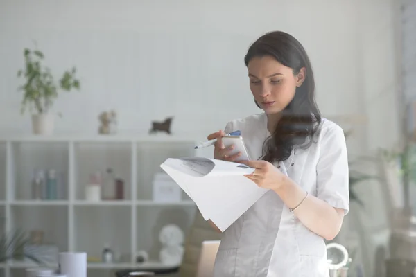 Doctor using mobile phone and holding papers — Stock Photo, Image