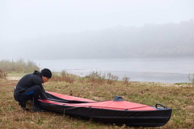 Nehir sisli, göl önünde kanocu güzel gökyüzü ve suyla, kanolu adam nehir kıyısında, aşırı hareketli, siyah spor elbiseli adam boş vakitlerini aktif olarak harcıyor..