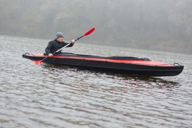 Soğuk bir sonbahar gününde kayak küreği tutan ve kanoyla gezen adama yakın, mesafeli görünüyor, su sporlarından hoşlanıyor, siyah ceket giyiyor..