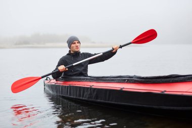 Genç ve çekici bir adam kanoyla eğleniyor. Nehirde kano süren, nehirde yelken açan, elinde küreği tutan, mesafeye bakan, soğuk, sisli bir günde kano süren çekici bir adam..