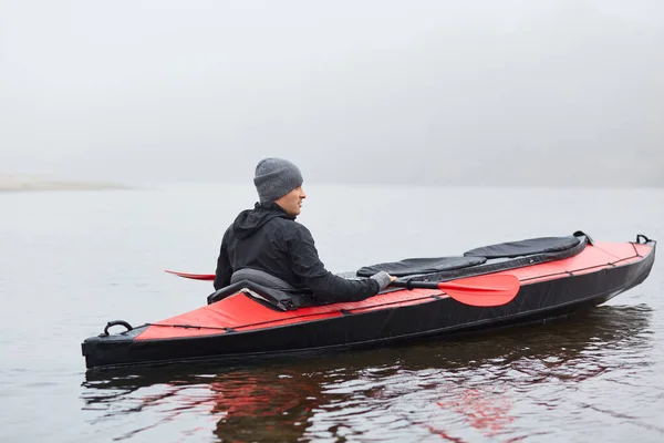 人们在河里或湖上划着皮划艇 观察大自然 穿着黑色夹克 头戴灰色帽子 户外雾蒙蒙的天气 参加水上运动的倒影 — 图库照片