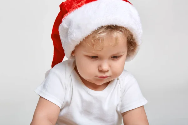 サンタクロースの赤い帽子の小さな赤ちゃんはクリスマス 赤い帽子の幼児 新年の休日 かわいい子供は離れて見て 白い背景の上に隔離されたポーズ — ストック写真