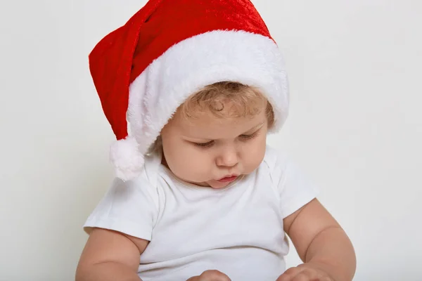 かわいい赤ちゃんは 彼の手の中に何かを注意深く見て 屋内で遊んでクリスマス服を着て金髪の波状の髪をしており 白い背景に隔離されたポーズを見て集中しています — ストック写真