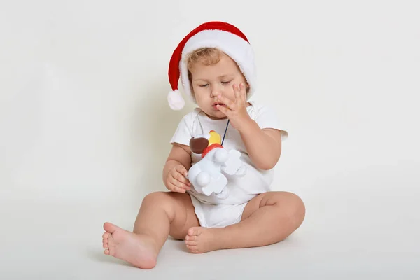 白い背景の床に座り裸足で体にフィットしクリスマスの帽子をかぶって白い壁の上に隔離された幼児 — ストック写真