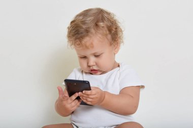 Yakışıklı sarışının yerde oturup akıllı telefonuyla oynayan, yeni teknolojileri öğrenen, cihaz ekranına ilgi duyan, cep telefonuyla çizgi film izleyen çocuk manzarası..