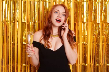 Ginger, elinde bir kadeh şampanya tutan, cep telefonuyla konuşan, şok edici haberler duyan, sarı arka planda süslerle süslenmiş, ağzı açık bir bayan, küçük siyah elbiseli genç kadını şok etti..
