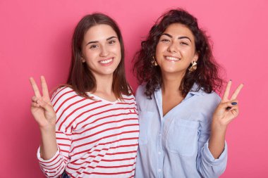 Pembe arka planda izole edilmiş iki kız arkadaş, dişlek tebessümle kameraya bakar ve zafer işareti gösterir, birbirlerine sarılırken mutluluklarını ifade ederler, kadın kıyafetleri gündelik kıyafetlerdir..