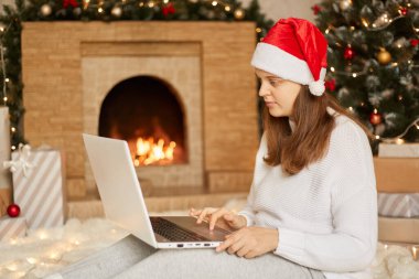 Noel internette, internet üzerinden çalışıyor. Video görüşmesi için dizüstü bilgisayar kullanan beyaz kız Noel Baba şapkası ve beyaz kazak giyiyor. Dizüstü bilgisayara bakan kadın şöminenin yanında oturuyor.