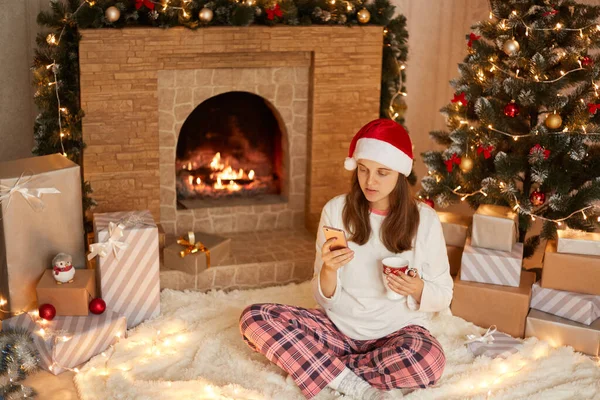 Ung Kvinna Bär Tomte Hatt Och Pyjamas Sitter Golvet Bland — Stockfoto