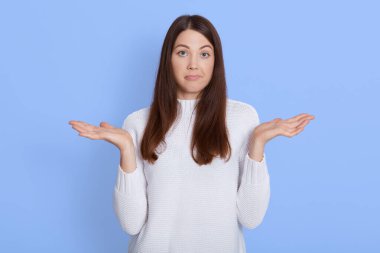 Kafası karışmış kadının kapalı çekimleri ellerini yana açıyor, şüpheli bir ifadeyle bakıyor, karar veremiyor, mavi arkaplanda poz veriyor, kafası karışmış bir kız kameraya bakıyor..