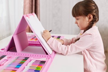 Masa başında oturmuş resim yapan küçük bir kız, yaratıcılık ve sanat setiyle resim çizen, at kuyruklu şirin bir ressamın yan görünüşü, mum boya kalemleriyle resim çizen bir çocuk..