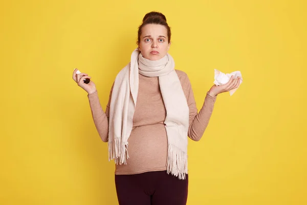 穿着米黄色毛衣和围巾的年轻漂亮的怀孕女孩使用治疗鼻塞的方法 让人心烦意乱的孕妇在黄色背景下显得孤立无援 — 图库照片