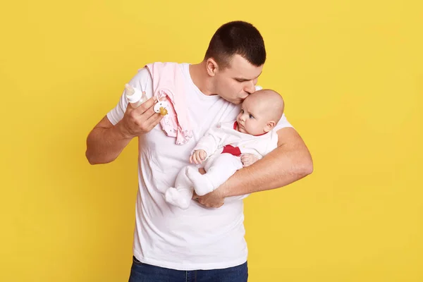 快乐的年轻父亲温柔地看着他的小女儿 吻着她的额头 孤零零地站在黄色的背景上 穿着白色休闲衫和他年幼的孩子在一起 — 图库照片