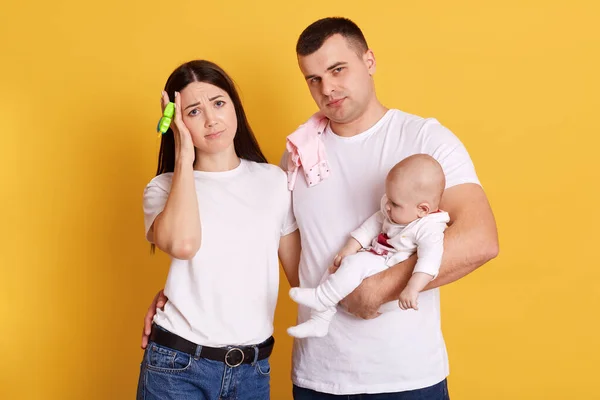 若いです両親無睡眠で新生児で夜疲れていると疲れ顔の表情 ママは頭痛の種 カップルとともに彼らの幼児のポーズ黄色の背景に隔離 — ストック写真