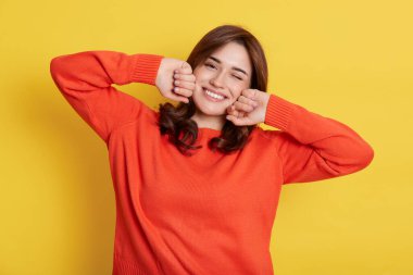 Uykudan sonra esneyen genç bir kadının portresi, mükemmel bir ruh haliyle uyanıyor, dişlek bir gülümsemeyle kameraya bakıyor, turuncu bir süveter giyiyor, yumruklarını yanaklarında tutuyor..