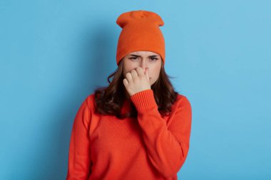 Tatminsiz kadın kaşlarını çatar, şapkalı kadın ve sıradan kazak kötü koku yüzünden burnu tutar, mavi arka planda tek başına durur, sevimli siyah saçlı kız iğrenç bir şey görür..