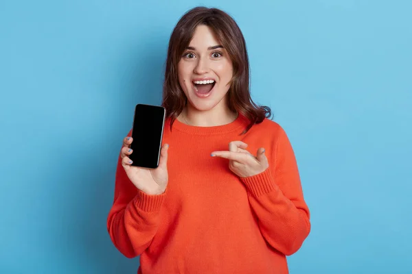 身着休闲装的女人的画像 在蓝色背景下显示出手机的空白屏幕 有着大大的张嘴和兴奋的表情的迷人女孩拿着手机指尖 — 图库照片
