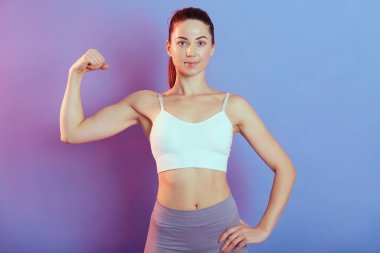 Ön manzara portresi. Çekici görünümlü, sevimli, sevimli, güçlü, neşeli, arka planda izole edilmiş kasları olan, kolsuz bluz ve tayt giyen bir kadın..