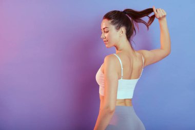 Güzel, bronz tenli bir kadın eğitimden sonra ara veriyor. Renkli arka planda izole edilmiş. Elini at kuyruğundan ayırmıyor..