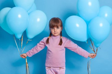Beyaz tenli çekici kadın çocuk doğum günü partisine gider, iki elinde mavi helyum balonları taşır, gül kazağı giyer, arka planda tek başına dolaşır..