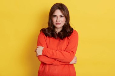 Güzel gülümseyen Avrupalı kadın kendini nazikçe kucaklıyor, kameraya bakıyor, kendini sevdiriyor, rahat hissediyor, iyi bir ruh hali içinde, sarı arka planda izole edilmiş..