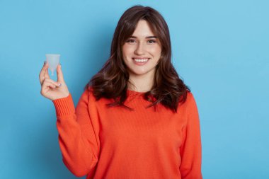 Çekici, koyu renk saçlı, elinde plastik bardakla gezen bir kadın. Mavi arka planda izole edilmiş, gülümseyen bir kadın. Dönem boyunca kişisel hijyen ürününü düşünüyor..