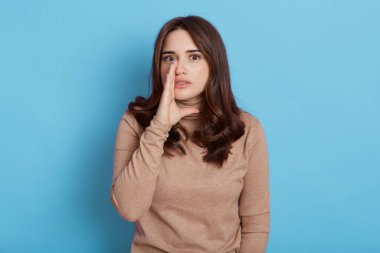 Şaşırmış meraklı kadın elini ağzının kenarında tutuyor ve fısıldıyor. Dedikodular yayıyor. Meraklı bir ifadeyle kameraya bakıyor..