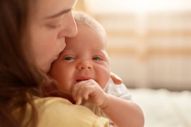 Annenin elinde yeni doğmuş bir bebekle profili, annesi küçük oğlunu ya da kızını nazikçe öpüyor, harika bir çocuk yumruğunu düzgün tutuyor ve kameraya bakıyor..