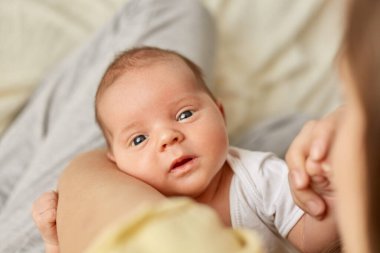 Yeni doğmuş bebek anne ellerinde, beyaz giysili küçük bir çocuk kameraya bakıyor, tuhaf bir yüz ifadesi var, etraftaki dünyayı inceliyor..