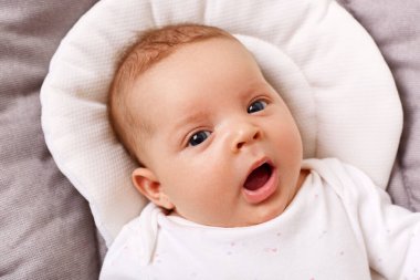 Gri battaniyenin üzerinde kameraya bakarak, ağzını açık tutarak, beyaz elbiseler giyerek, dünyanın dört bir yanını inceleyen sevimli bir kız çocuğu..