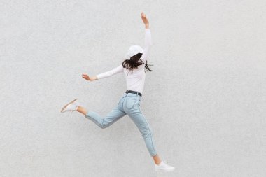 Kendine güvenen güzel bir kadın ayakta duruyor ve başka tarafa bakıyor, pozitif duygularını ifade ediyor, mutlu bir şekilde gülüyor, kot pantolon giyiyor, rahat bir gömlek ve beyzbol şapkası giyiyor, aydınlık duvarın üzerinde izole edilmiş..