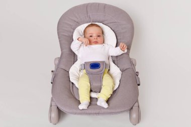 Çocuk merkezinde yatan yeni doğmuş şirin bir bebek, beyaz gömlek ve sarı pantolon giyen küçük bir kız, gri şezlongda sallanan bir bebek, beyaz arka planda izole edilmiş..