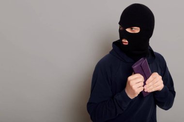Siyah kapüşonlu bir hırsız, bir cüzdan çaldı ve arkasına bakmadan kaçtı, yakalanmaktan korktu, uzayı kopyaladı, gri arka planda izole edildi..