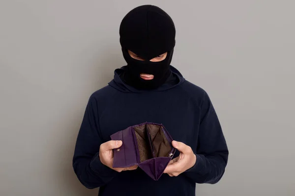 身穿黑色帽衫 戴着抢劫面具 手里拿着一只偷来的空皮夹 一副心烦意乱 孤立无援的样子 — 图库照片